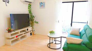 A living room with a flat-screen TV, a green sofa, a small round table, and a potted plant.