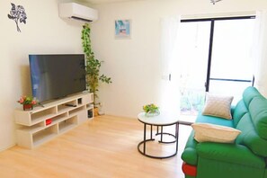 A living room with a flat-screen TV, a green sofa, a small round table, and a potted plant.