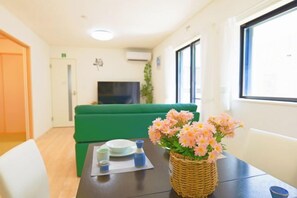 A room with a green sofa, a dining table with a vase of flowers, and a television in the background. - Tsukuba Garden House QIAO No.361 (Tsukuba)