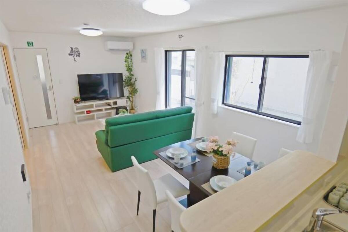 Un soggiorno moderno con un divano verde, un tavolo da pranzo con sedie, una televisione e una finestra con tende.