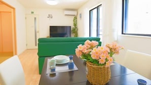 Ein Zimmer mit einem grünen Sofa, einem Esstisch mit Blumenvase und einem Fernseher im Hintergrund.