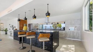 A modern kitchen with a central island, bar stools, pendant lighting, and a view of the outdoors. - Villa Spice Samui (Koh Samui)