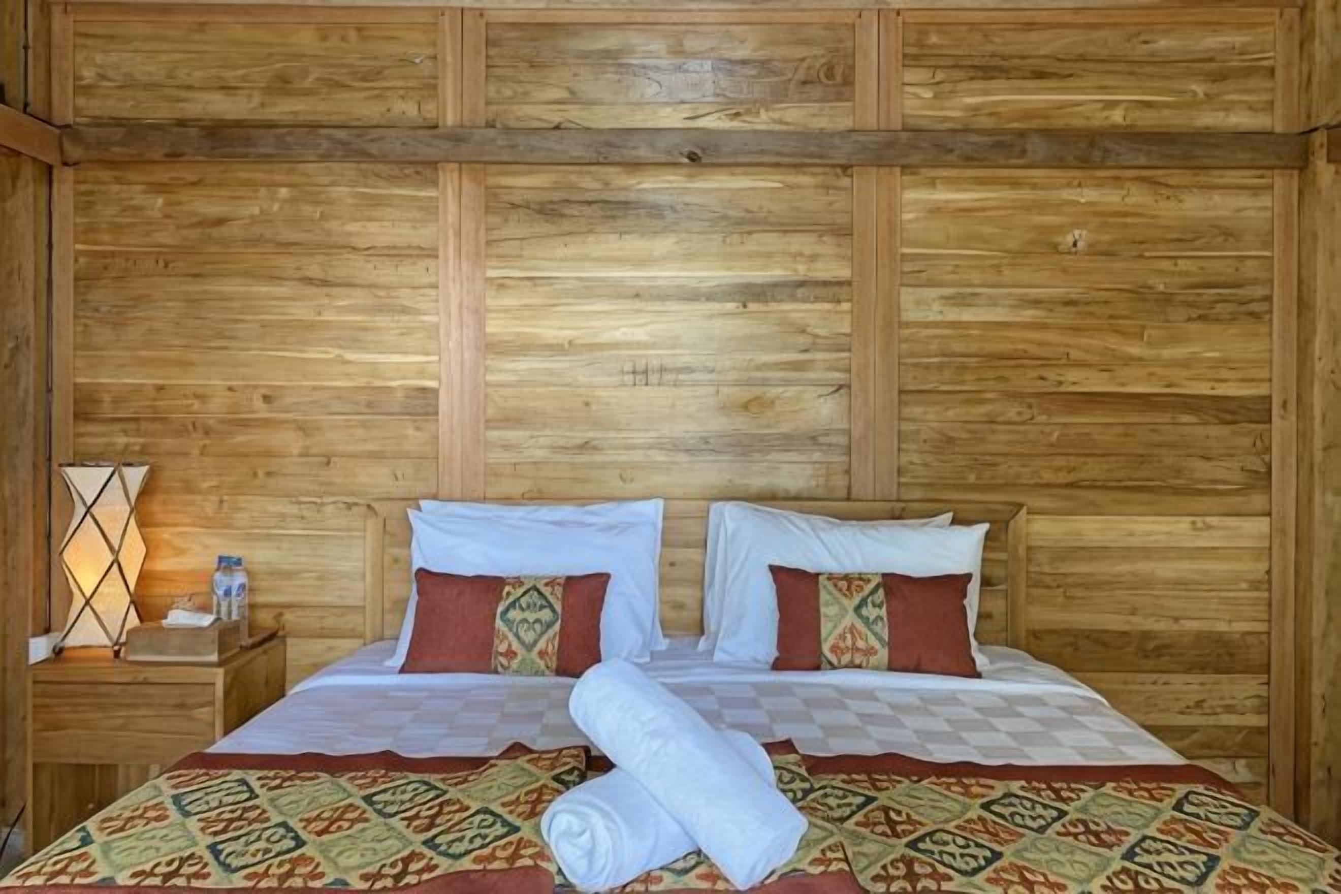 A wooden-paneled room with a bed, pillows, a nightstand, and a lamp.