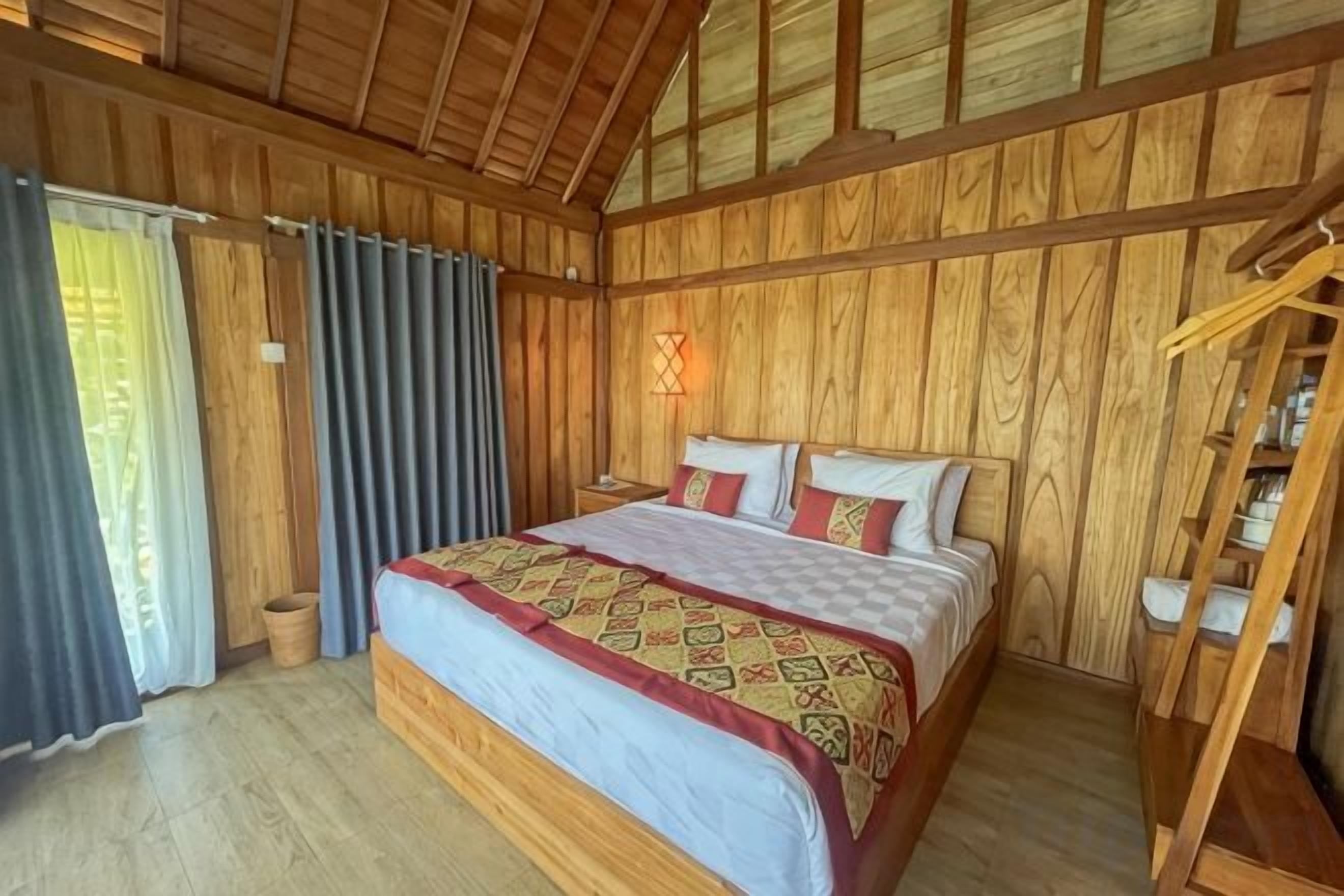 A wooden-paneled room with a bed, a nightstand, and a wardrobe.
