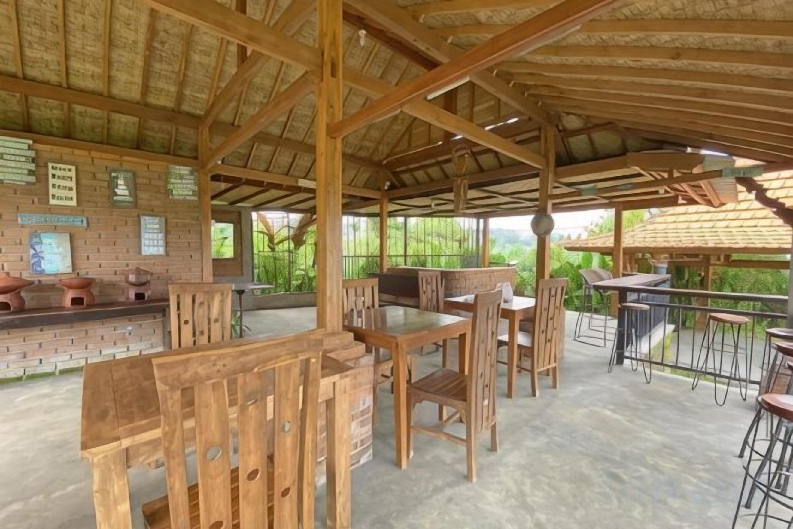 An outdoor wooden structure with tables and chairs, a brick wall with signs, and a view of greenery.