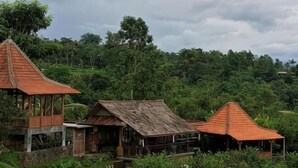 A traditional wooden house with a thatched roof, surrounded by lush greenery and a hilly landscape. - Jatiluwih Guava Eco Living Managed by Manara (Bali)