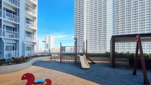 Un parque infantil con tobogán y columpios, rodeado de edificios altos.