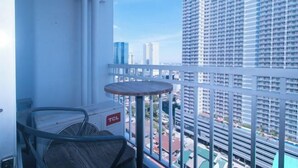 Un balcón con vistas a edificios altos, una mesa redonda pequeña y un ventilador.