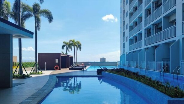 Zona de piscina con vistas despejadas al océano, un edificio con balcones y palmeras.