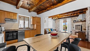 A modern kitchen with wooden cabinets, a dining area with a large table, and a stone fireplace. - Villa Lara with Private Pool near Pula (Čabrunići)