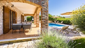 A covered patio area with a pool, wicker furniture, and a stone wall. - Villa Lara with Private Pool near Pula (Čabrunići)