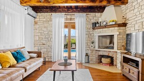A cozy living room with a stone fireplace, leather sofa, and a wooden table. - Villa Lara with Private Pool near Pula (Čabrunići)