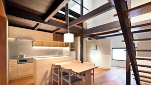 A modern kitchen with wooden cabinets, a dining area with a table and chairs, and a loft-style ceiling with exposed beams. - Kyo No Ondokoro Goshonishi #6 (Kyoto)