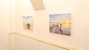 Un couloir orné d’œuvres d’art sur les murs, doté d’un plancher en bois et d’un luminaire.