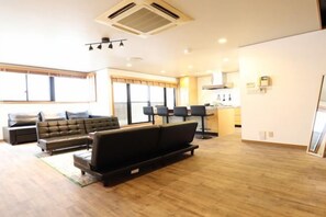 A spacious living room with a sofa, a coffee table, and a dining area with chairs. - Crane Court KitaHorie (Osaka)