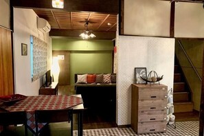 Una stanza con un letto, un tavolo con tovaglia fantasia, un comò e una scala.