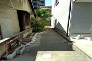A narrow alleyway with a concrete path, a small planter with plants, and a wooden crate labeled 'SEIBOTA'. - Tsukamoto Collector (Osaka)