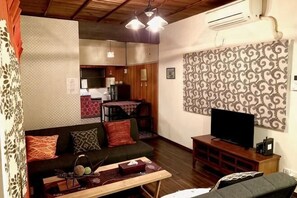 Una sala de estar con sofá, televisión, mesa y una cocina al fondo.