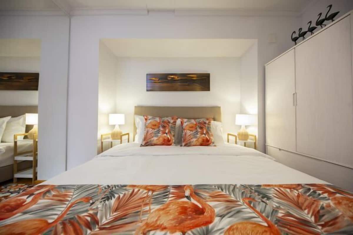 A hotel room with a bed, two bedside tables, a headboard, a wardrobe, and a painting on the wall.