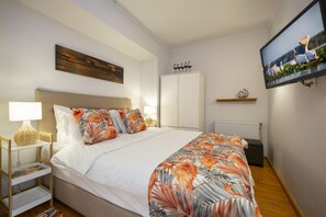 A bedroom with a bed, a TV mounted on the wall, a wooden nightstand, and a shelf with a decorative item. - FlamingoHaven Chic&Renovated 1BRwBalcony PrimeSpot (Bucharest)