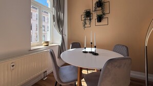 Un'area pranzo con un tavolo rotondo, sedie grigie, una finestra vista edifici e fioriere a parete.