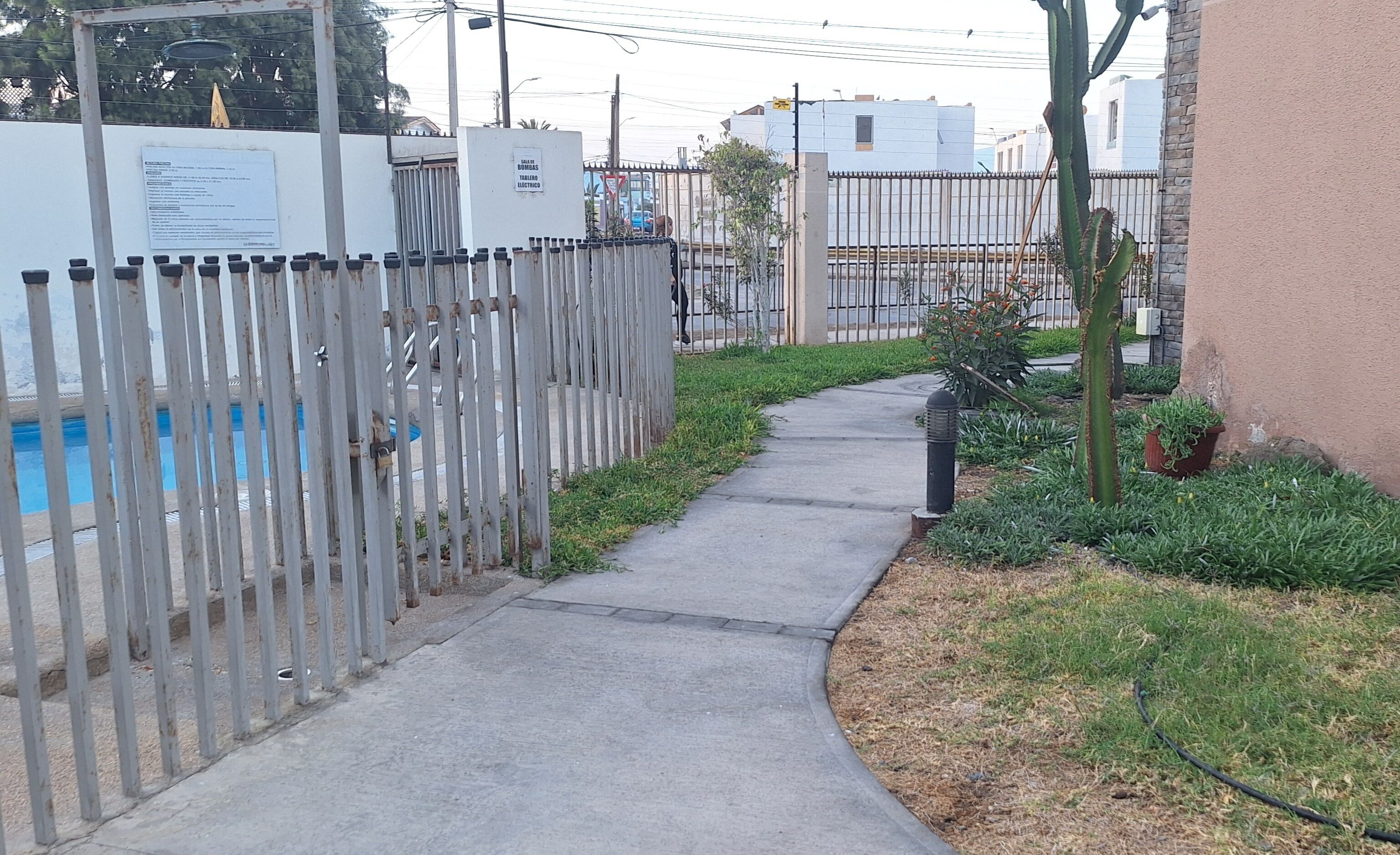 A pathway leading to a pool area, surrounded by a fence and greenery.