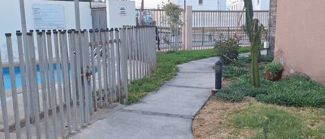 A pathway leading to a pool area, surrounded by a fence and greenery.