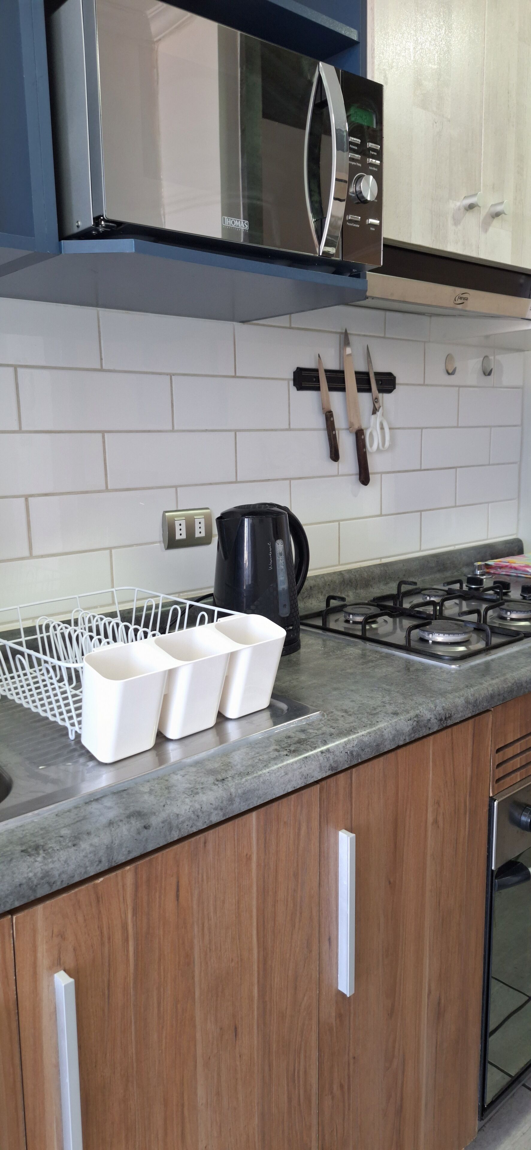 Una cocina con salpicadero de azulejos blancos, microondas, cocina a gas y cafetera.
