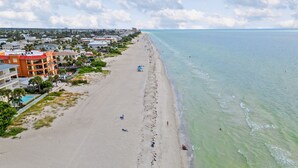 Una playa con una hilera de edificios, incluyendo un hotel de varios pisos y balcones, y una vista despejada del océano.