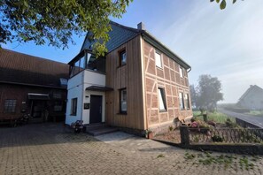 A two-story house with a brick facade and a sloped roof, a paved driveway, and a fenced garden area. - LiFarm.de Apartments (Aerzen)