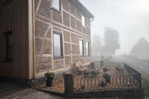 A brick building with a wooden door and windows, a paved entrance, and a metal fence. - LiFarm.de Apartments (Aerzen)