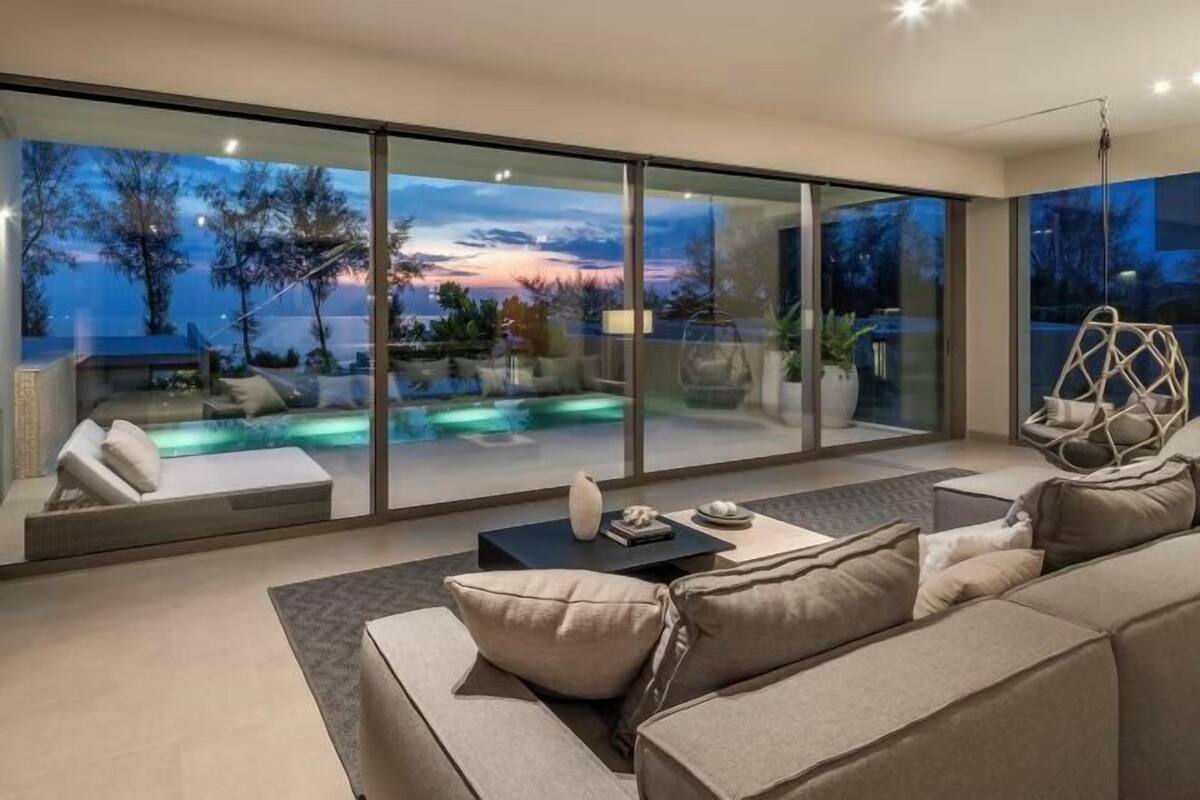 A modern living room with a large glass wall, a sofa, a coffee table, and a hanging chair.