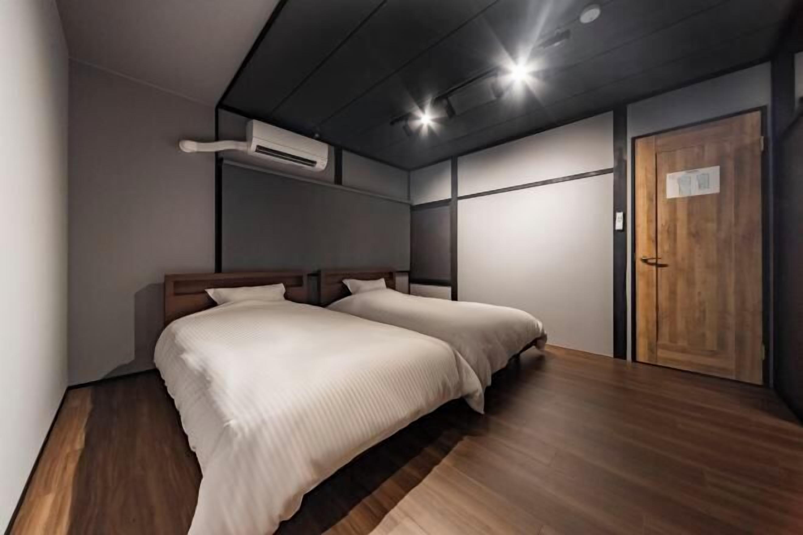 Ein modernes Schlafzimmer mit zwei Betten, Holzboden, einer Holztür und einer Klimaanlage.