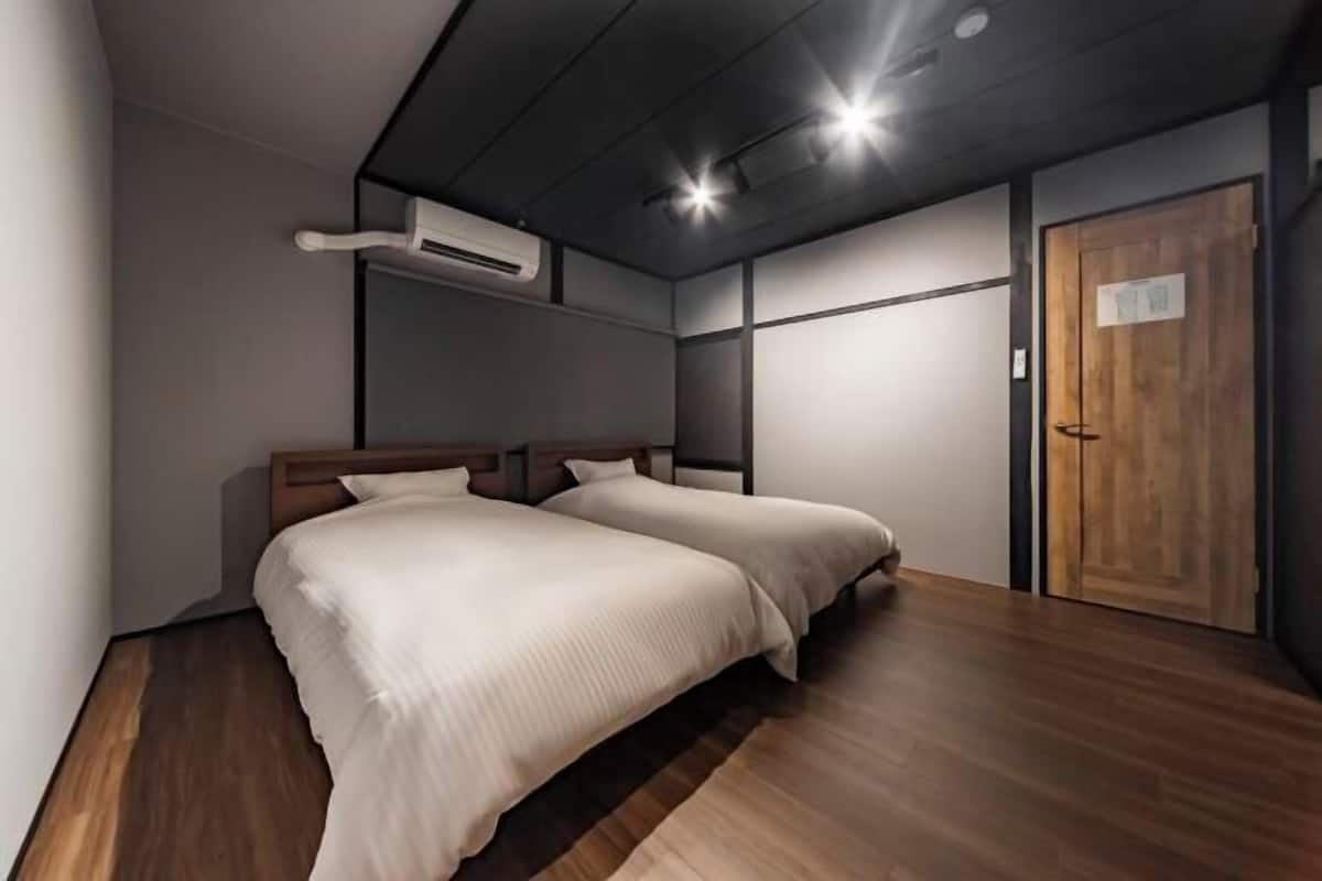 A modern bedroom with two beds, wooden flooring, a wooden door, and an air conditioning unit.