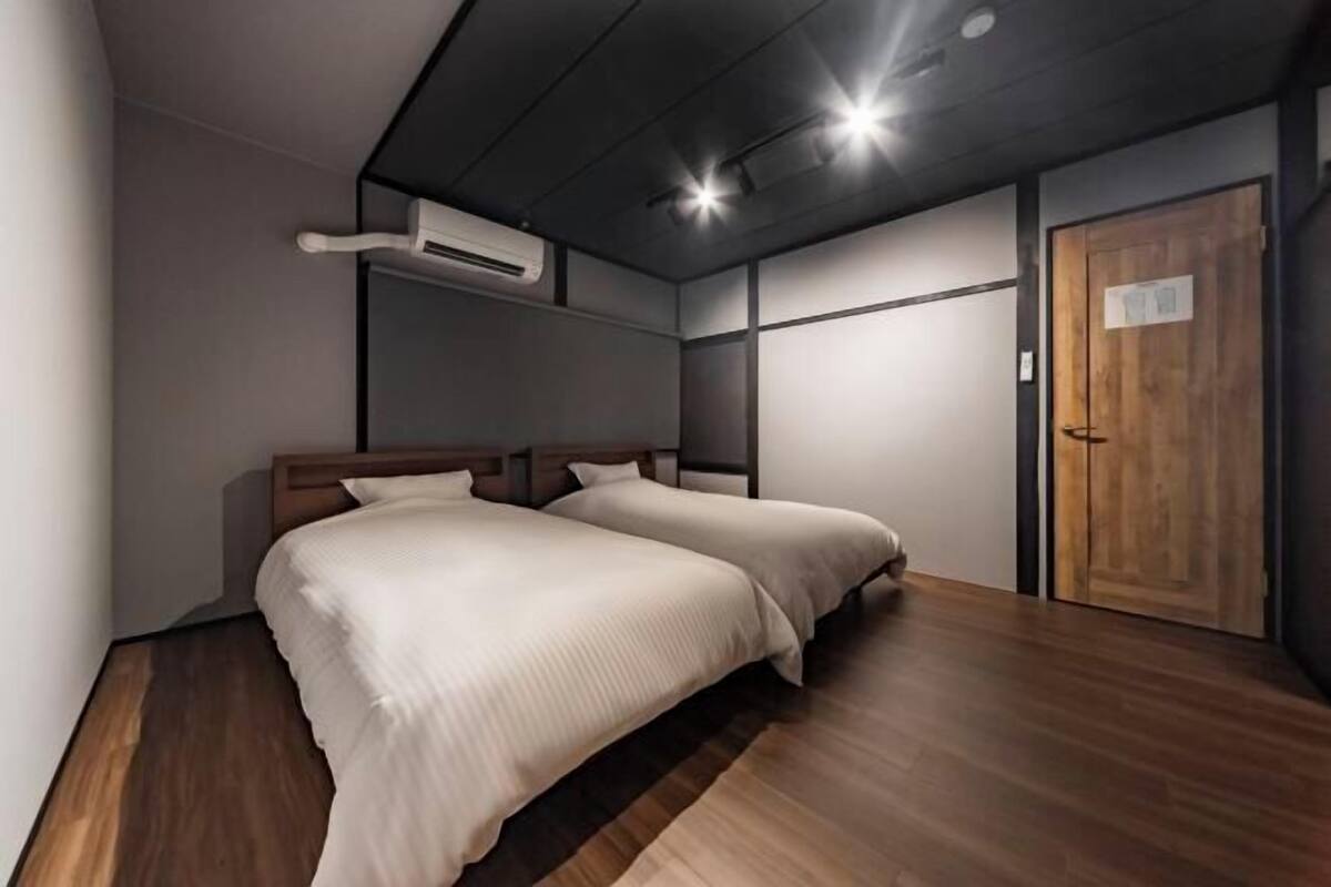 Un dormitorio moderno con dos camas, suelo de madera, una puerta de madera y un equipo de aire acondicionado.
