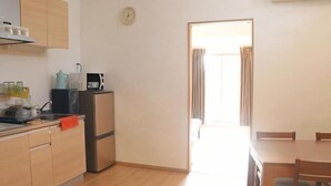 A compact kitchen with wooden cabinets, a refrigerator, and a dining area with a table and chairs. - Shikai Family (101) (Osaka)