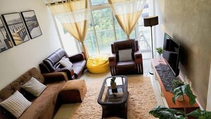 A living room with a brown leather sofa, a yellow bean bag, a brown armchair, a glass coffee table, and a TV on a stand. - Putrajaya Dwiputra 6 Plus 1 PAX Fully Air-Con (Putrajaya)