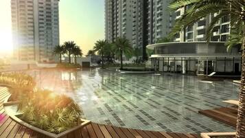 A swimming pool area with tiled flooring, wooden deck, and palm trees.