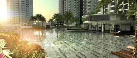 A swimming pool area with tiled flooring, wooden deck, and palm trees.