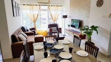 Un comedor con una mesa preparada para cuatro personas, un sofá, un televisor y una planta.