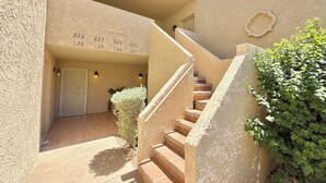 A building entrance with numbered doors, a staircase, and a small garden area.