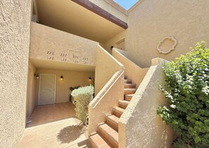 A building entrance with numbered doors, a staircase, and a small garden area.