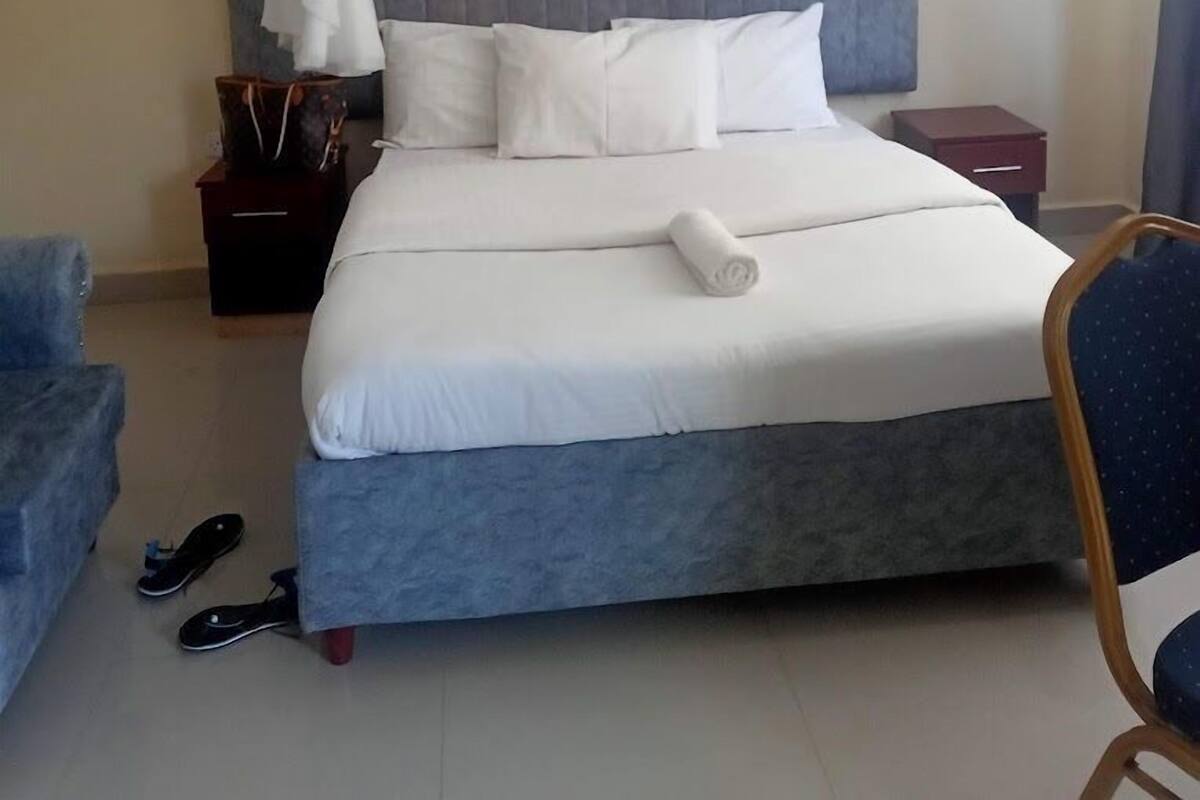 Een hotelkamer met een bed, een nachtkastje, een stoel en een paar slippers op de vloer.