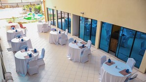 Un espace extérieur aménagé en terrasse, avec des tables et des chaises rondes, recouvertes de nappes blanches et de serviettes bleues.