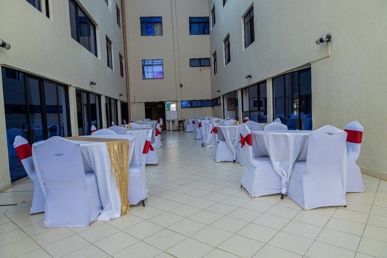 A spacious indoor area with rows of tables and chairs, each set with white tablecloths and red sashes.