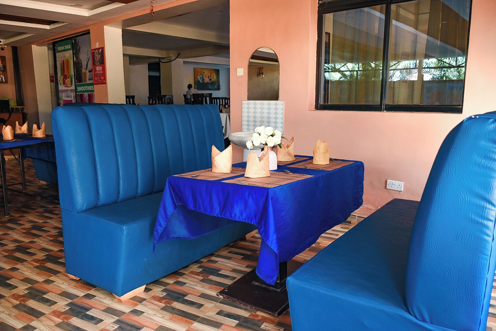 A restaurant with blue cushioned seating and a table set with a white vase and napkins.
