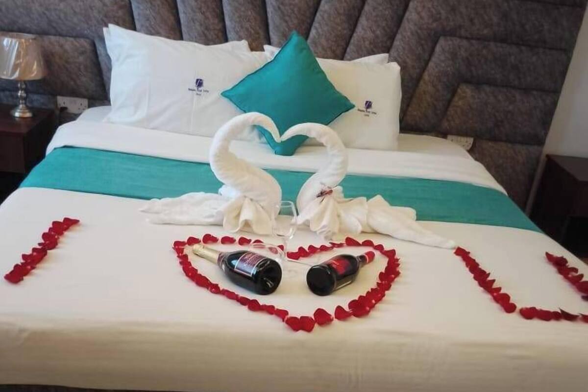 Een net opgemaakt bed met een hartvormige bloemstelling van rozenblaadjes en een fles, vermoedelijk een decoratieve opstelling.