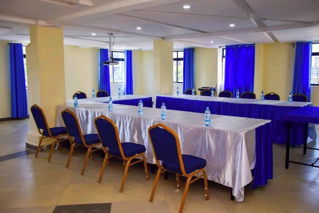 Une salle de conférence avec une longue table, des chaises bleues et des bouteilles d’eau.