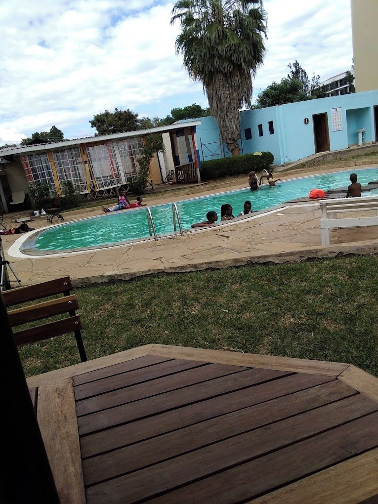 A pool area with a wooden deck, a palm tree, and a building with a blue facade in the background.