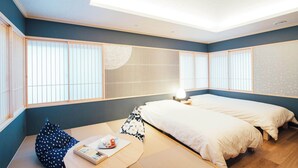 Une pièce avec un sol recouvert de tatamis, un lit avec une literie blanche, une petite table avec une lampe et des paravents en papier de riz (shoji).
